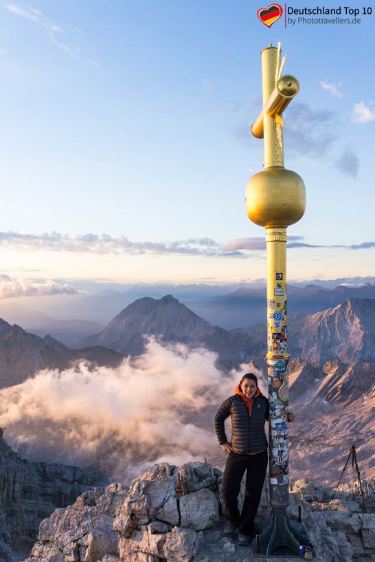 Reisebloggerin Biggi Bauer am Gipfel der Zugspitze mit dem goldenen Gipfelkreuz